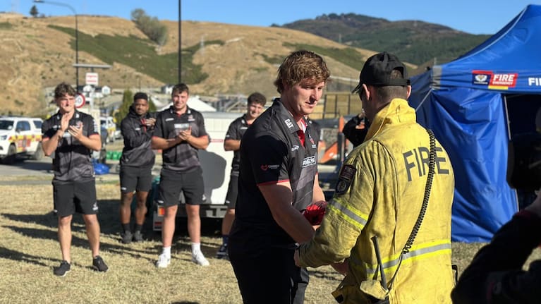 Crusaders player Cullen Grace hands over a jersey to a firefighter.