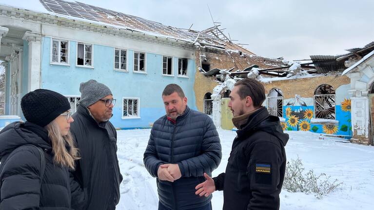 Defence Minister Peeni Henare speaks with his Ukrainian counterpart in front of buildings damaged in the Russian invasion of Ukraine.