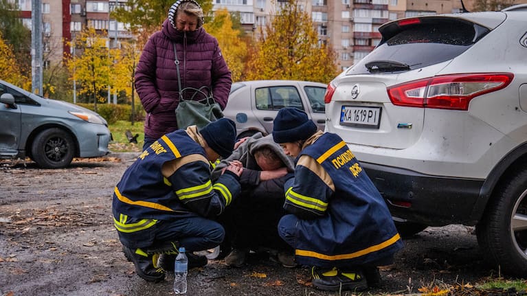 Emergency workers comfort a man who lost his son in Russia's drone attack that hit residential buildings in Kyiv, Ukraine.