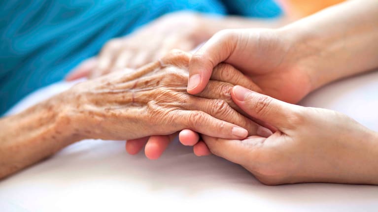 Woman holding senior woman's hand on bed.