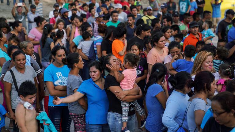 Migrants, many who were returned to Mexico under the Trump administration’s “Remain in Mexico,” program wait in line to get a meal in an encampment near the Gateway International Bridge in Matamoros.