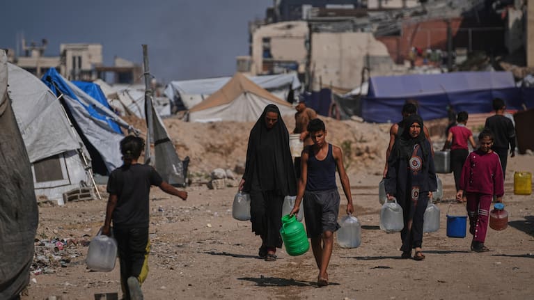 Palestinians carry jerrycans and plastic bottles with water after collecting it at a camp for displaced people in Gaza City