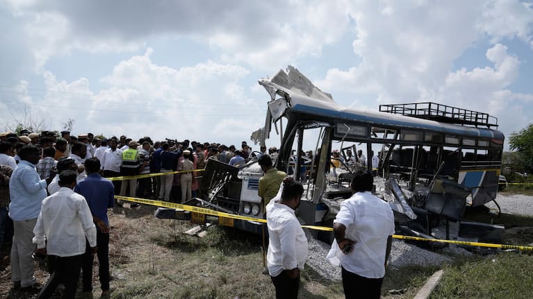 People stand next to the passenger bus after a truck loaded with concrete stone chips rammed into it at Chevella in southern state of Telangana, India.
