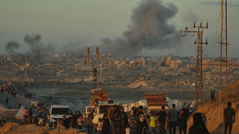 Smoke rises following an Israeli military strike in the background as displaced Palestinians flee northern Gaza, carrying their belongings along the coastal road near Wadi Gaza, Wednesday, October 1, 2025.